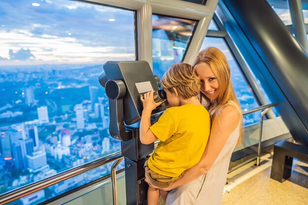 Mamá e hijo están mirando el paisaje urbano de Kuala Lumpur Use binoculares Vista panorámica del horizonte de la ciudad de Kuala Lumpur por la noche en el edificio de rascacielos al atardecer en Malasia Concepto de viaje con niños