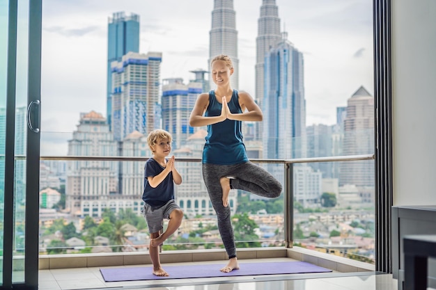 Mamá e hijo están practicando yoga en el balcón en el fondo de una gran ciudad mamá deportiva con niño