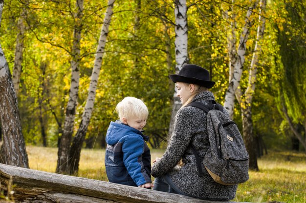 Mamá e hijo están sentados en el bosque de otoño en un tronco.