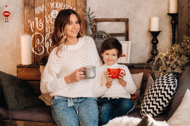 Mamá e hijo están sentados en casa en el sofá con un regalo y café en sus manos. Familia feliz