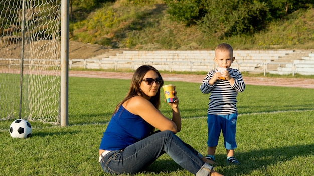 Mamá e hijo jugando al fútbol se toman un descanso para disfrutar de un refrigerio frente a los postes de la portería.