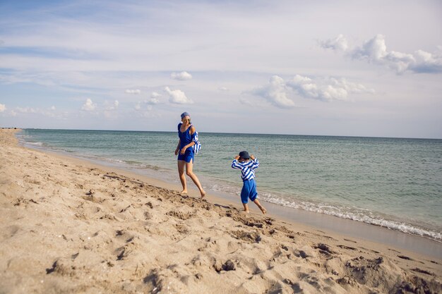 Mamá e hijo en ropa azul corren al mar de la playa en verano durante las vacaciones