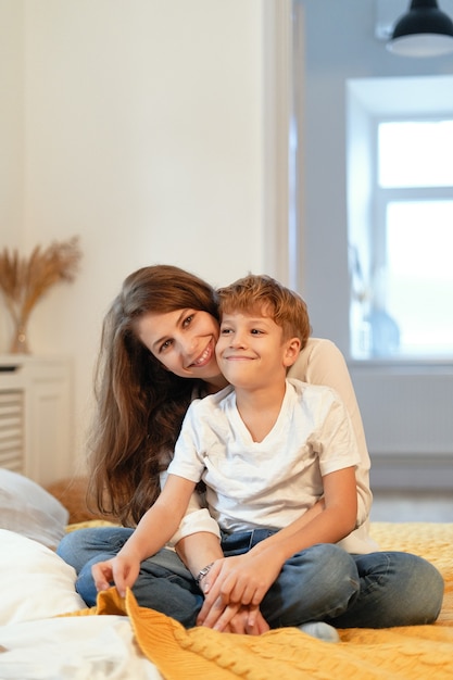 Mamá e hijo sonriendo, abrazándose, divirtiéndose, pasando tiempo juntos en un ambiente relajante en casa mientras están sentados