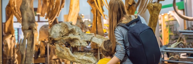 Mamá e hijo viendo esqueleto de dinosaurio en formato largo de pancarta de museo
