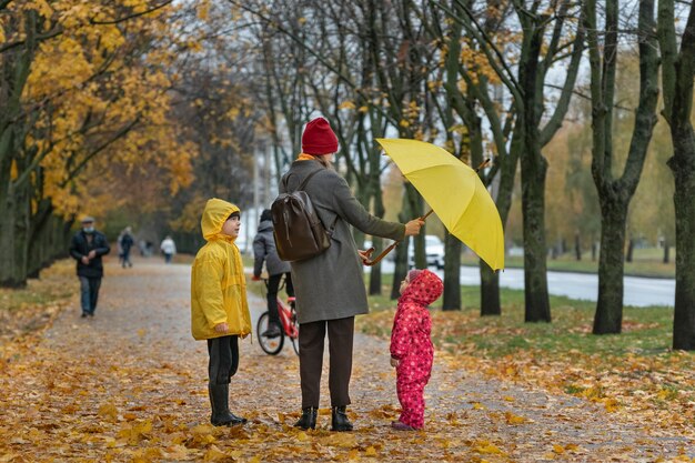 Mamá e hijos están caminando en el parque de otoño. Hojas amarillas caídas. Vista trasera