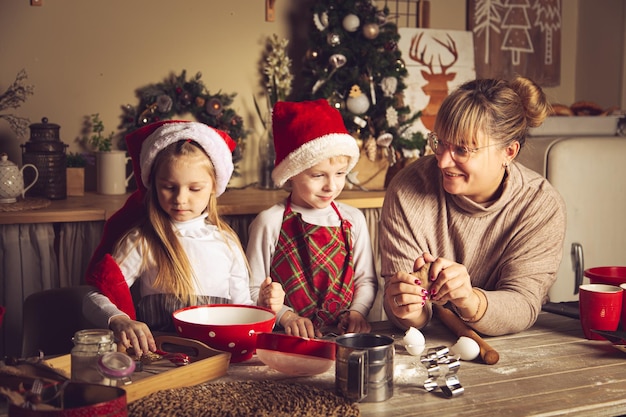 Mamá e hijos están preparando galletas en la cocina. Adornos navideños, tradiciones familiares, comida navideña, vísperas de vacaciones.