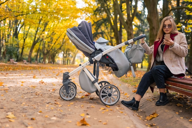 Mamá elegante con cochecito en el parque otoño