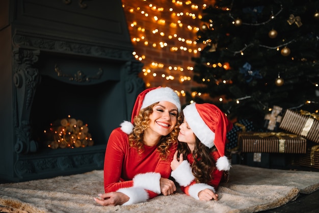 Mamá elegante con hija pequeña en trajes de Navidad cerca del árbol de Navidad. Feliz Navidad.