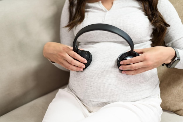 Mamá embarazada con auriculares en la barriga sentada en el sofá charlando con el bebé