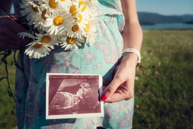 Mamá embarazada esperando en el campo de verano El concepto y la idea de la felicidad de la salud y la foto de ultrasonido de maternidad del bebé por nacer