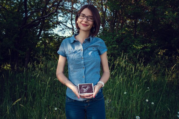 Mamá embarazada esperando en el campo de verano El concepto y la idea de la felicidad de la salud y la foto de ultrasonido de maternidad del bebé por nacer