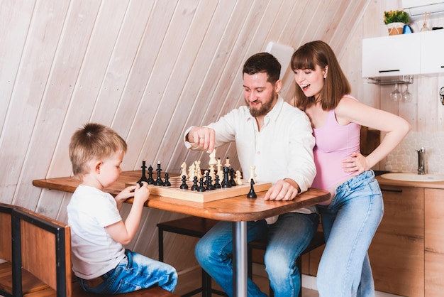 Mamá embarazada viendo a papá e hijo jugar al ajedrez en la mesa