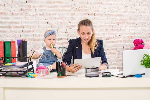 Mamá y empresaria trabajando con computadora portátil en casa y jugando con su bebé.