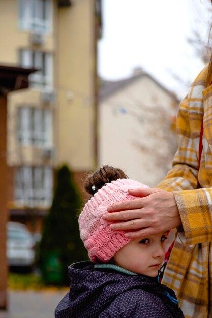 Mamá endereza el sombrero y el cabello de su hija durante una caminata otoñal colores de otoño