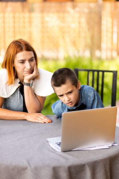 Mamá enseña al niño en casa en el jardín, educación en casa. Mamá ayuda a su hijo a hacer los deberes, el estrés. Lecciones escolares en línea a través de una computadora portátil