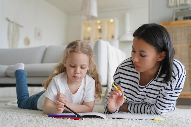 Mamá enseña a su hija pequeña a dibujar con lápices de colores tirados en el suelo en casa Creatividad infantil