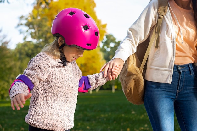 Mamá enseña a su pequeña hija a patinar en el parque de otoño