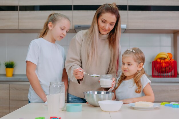 Mamá les enseña a sus hijas a cocinar masa en la cocina.