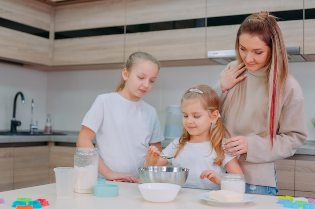 Mamá les enseña a sus hijas a cocinar masa en la cocina.