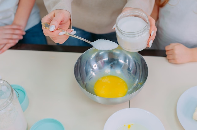 Mamá les enseña a sus hijas a hacer masa en la cocina y a batir huevos.