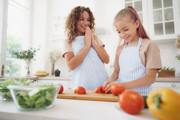 Mamá enseñando a su hija adolescente a cocinar ensalada de verduras en la cocina