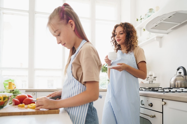 Mamá enseñando a su hija adolescente a cocinar ensalada de verduras en la cocina