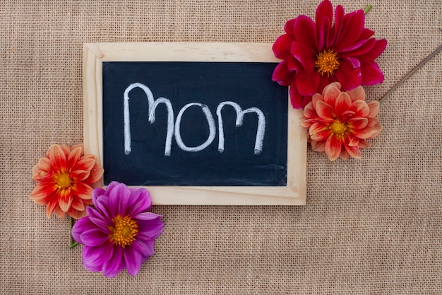 Foto mamá escrita en tabla de tiza con flores frescas en un fondo de tela rústica