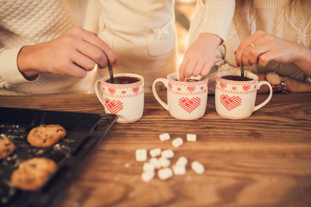 Mamá de familia, papá e hija en suéteres blancos cocinan y beben cacao con malvaviscos