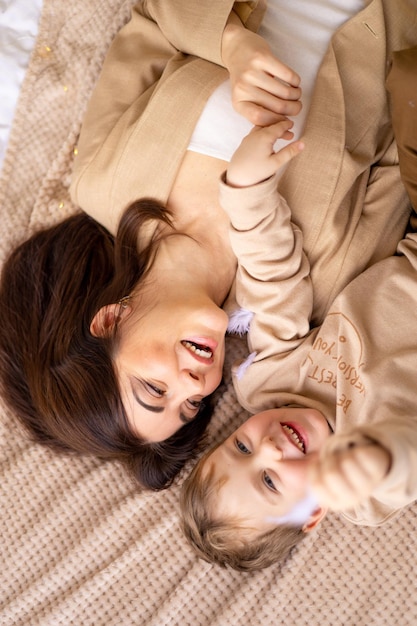 Mamá feliz abraza y besa a un niño pequeño en la cama en tonos naturales marrones beige divirtiéndose