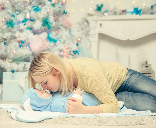 Mamá feliz y bebé en la sala de estar en la víspera de Navidad