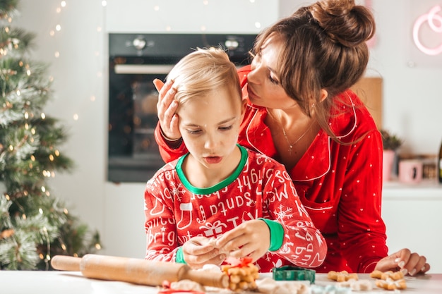 Mamá feliz besa a un niño en la cocina que prepara galletas para navidad