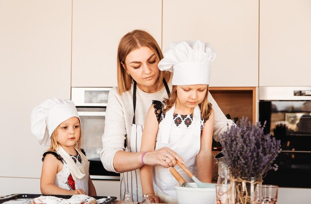 Mamá feliz y dos hijas parados juntos en la cocina se preparan y están listos para aprender a hacer panadería. idea de relación familiar.