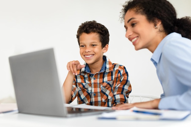 Mamá feliz enseñando a su hijo pequeño en la computadora portátil en casa