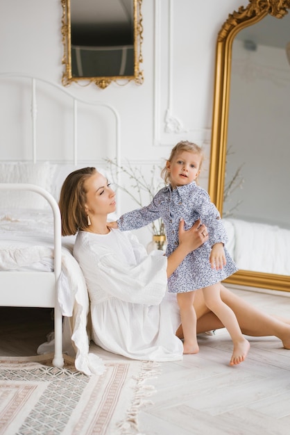 Mamá feliz está sentada junto a la cama y quiere abrazar a su hija