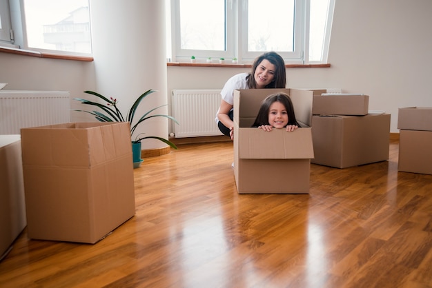 Mamá feliz con hija o niño se mudan a la casa y se divierten desempacando todo en cajas