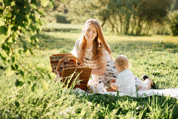 Mamá feliz con hija pequeña se sienta en un césped verde en el parque en un picnic con cestas día de la familia de padres con hijos