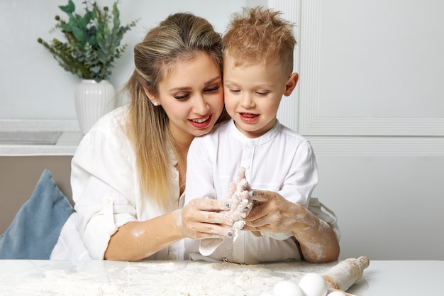 Mamá feliz limpia suavemente las manos de sus hijos de la masa pegada a ellos