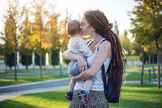 Mamá feliz moderna joven con el hijo del bebé que camina en Sunny Park