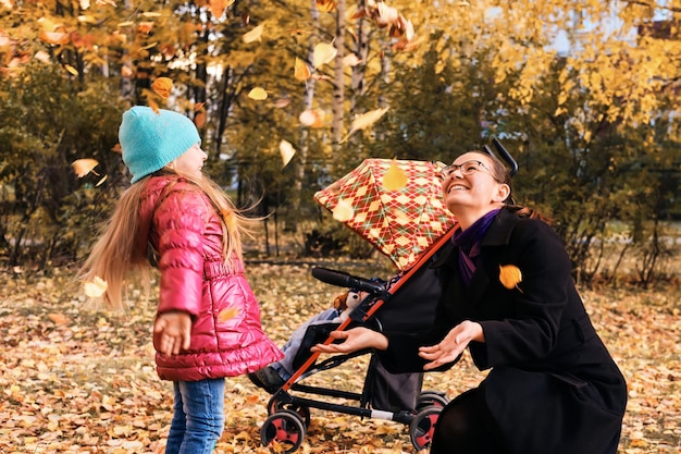 Mamá feliz y niños en un paseo en otoño juegan con hojas