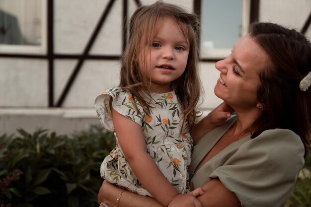 Mamá feliz sosteniendo a su pequeña hija en sus brazos y sonriendo al aire libre