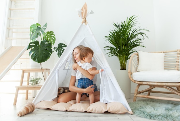 Mamá feliz y su hija jugando en el wigwam en casa