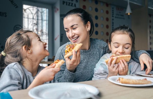 Mamá feliz y sus dos hijas comen pizza