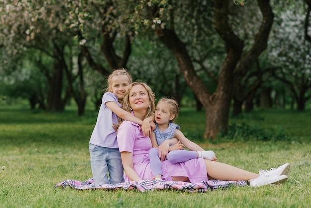 Mamá feliz y sus hijas se relajan en el parque en verano sentadas en una manta