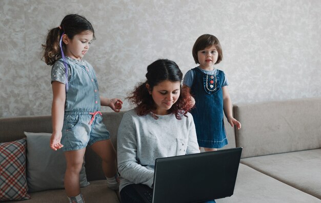 Mamá feliz trabajando en casa en la computadora rodeada de niños pequeños