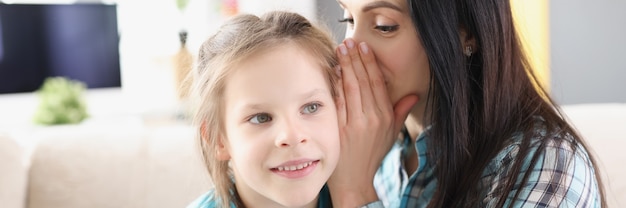 Mama flüstert dem kleinen Mädchen ein Geheimnis ins Ohr