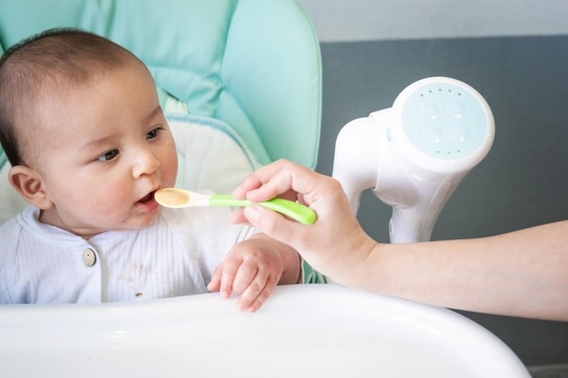 Mama füttert das Baby mit einem Löffel Gemüsepüree am Futtertisch der Kinder Appetit des Babys gesunde Ernährung Einführung von ergänzenden Lebensmitteln Copyspace Mock-up