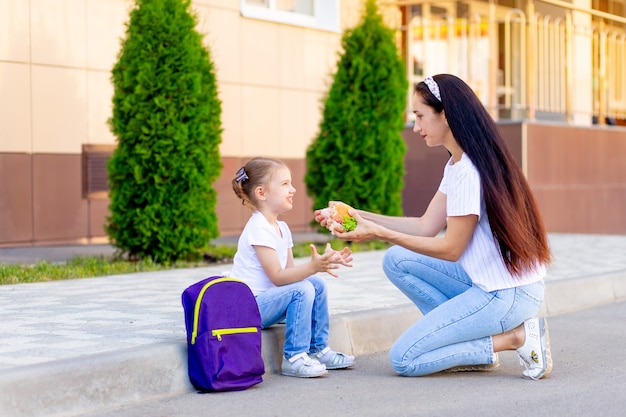 Mama füttert das Kind vor dem Schulessen oder einem Burger-Snack mit einem Schulmädchen, dem Konzept des Schulanfangs oder der Ernährung von Schulkindern