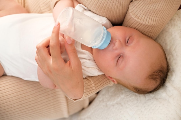 Mama füttert ein neugeborenes Baby mit einer Flasche, die Sonne scheint im Hintergrund