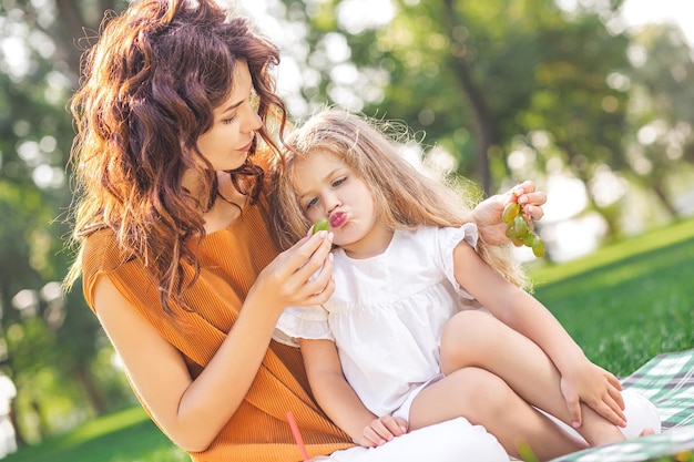 Mama füttert ihr Mädchen tagsüber im Park mit Trauben