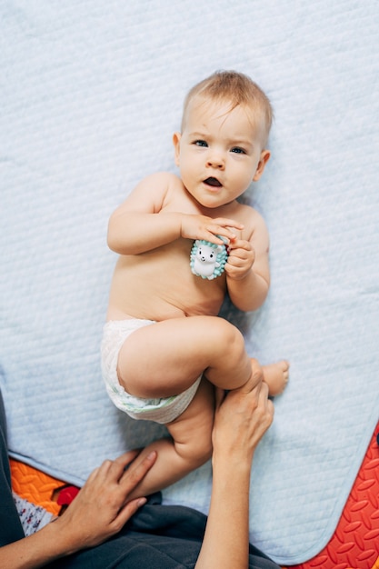 Mama hält Baby in einer Windel mit einem Spielzeug-Igel in den Händen an den Beinen Baby liegt auf einer Tagesdecke